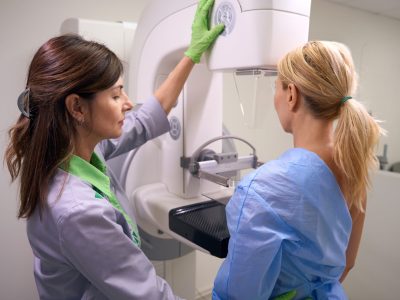 Radiographer using control panel for positioning compression paddle of mammography machine against client chest wall